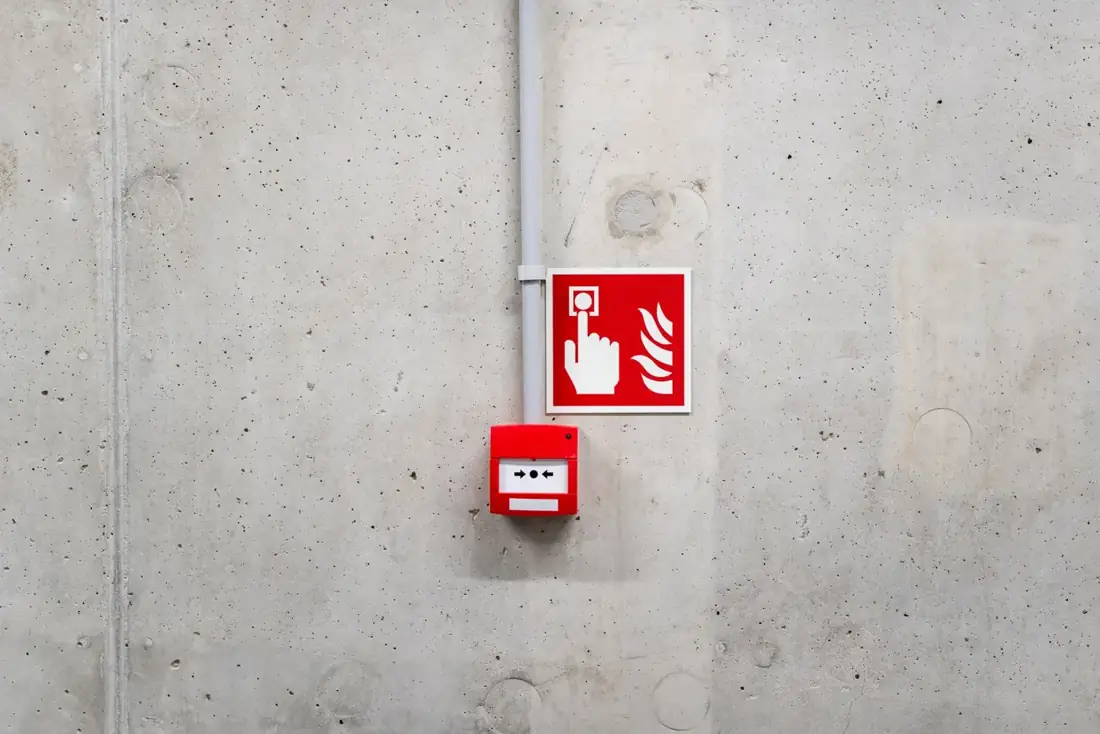 Fire alarm call point with conduit and fire safety sign on a commercial wall