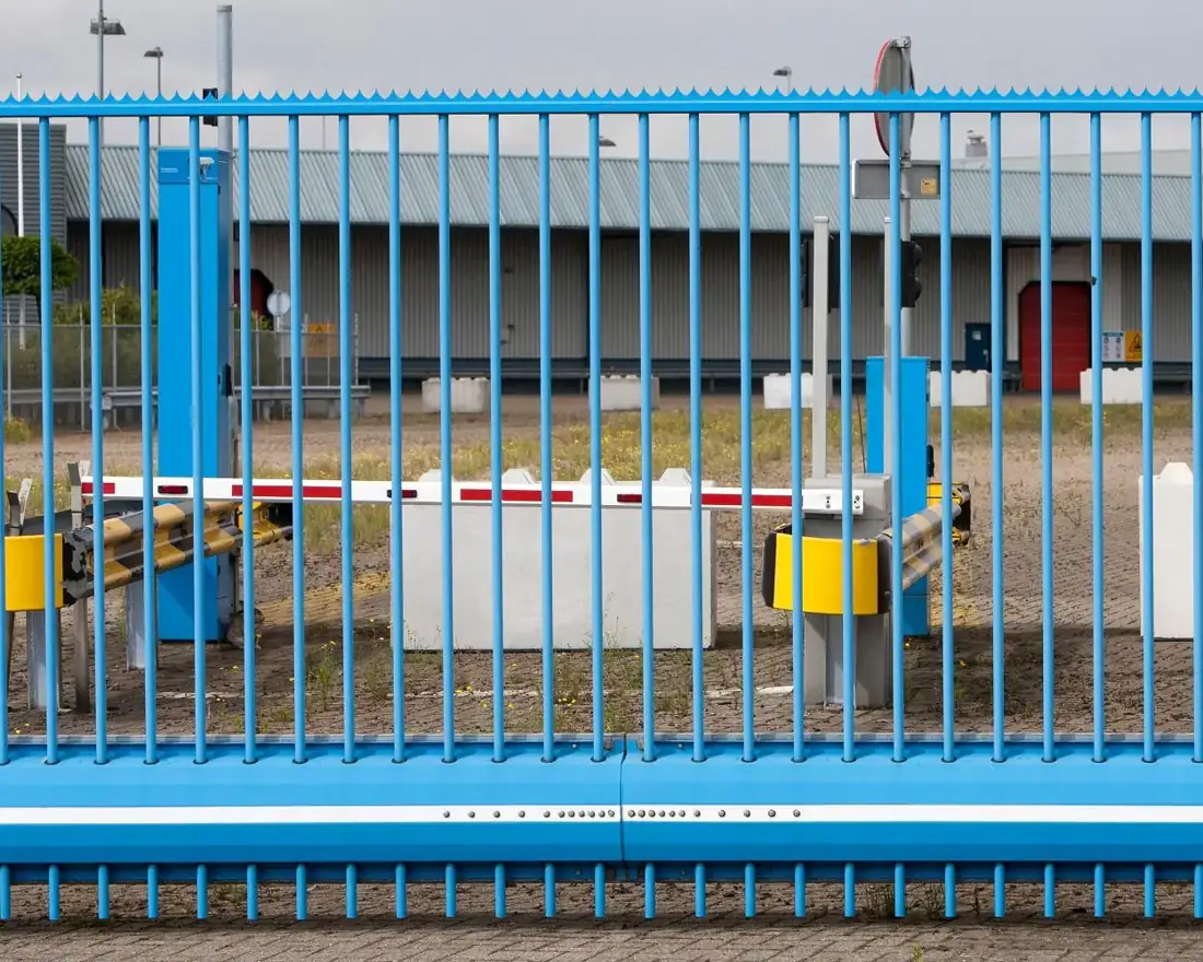 Automatic barrier at an industrial site entrance behind a blue steel security gate