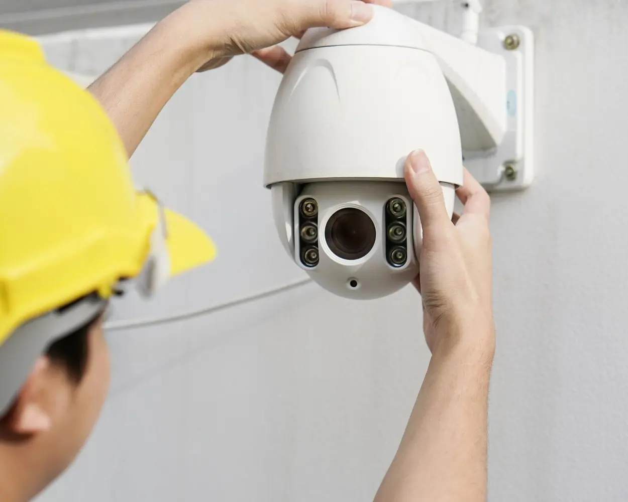 Engineer in a hard hat fitting a dome security camera to a wall