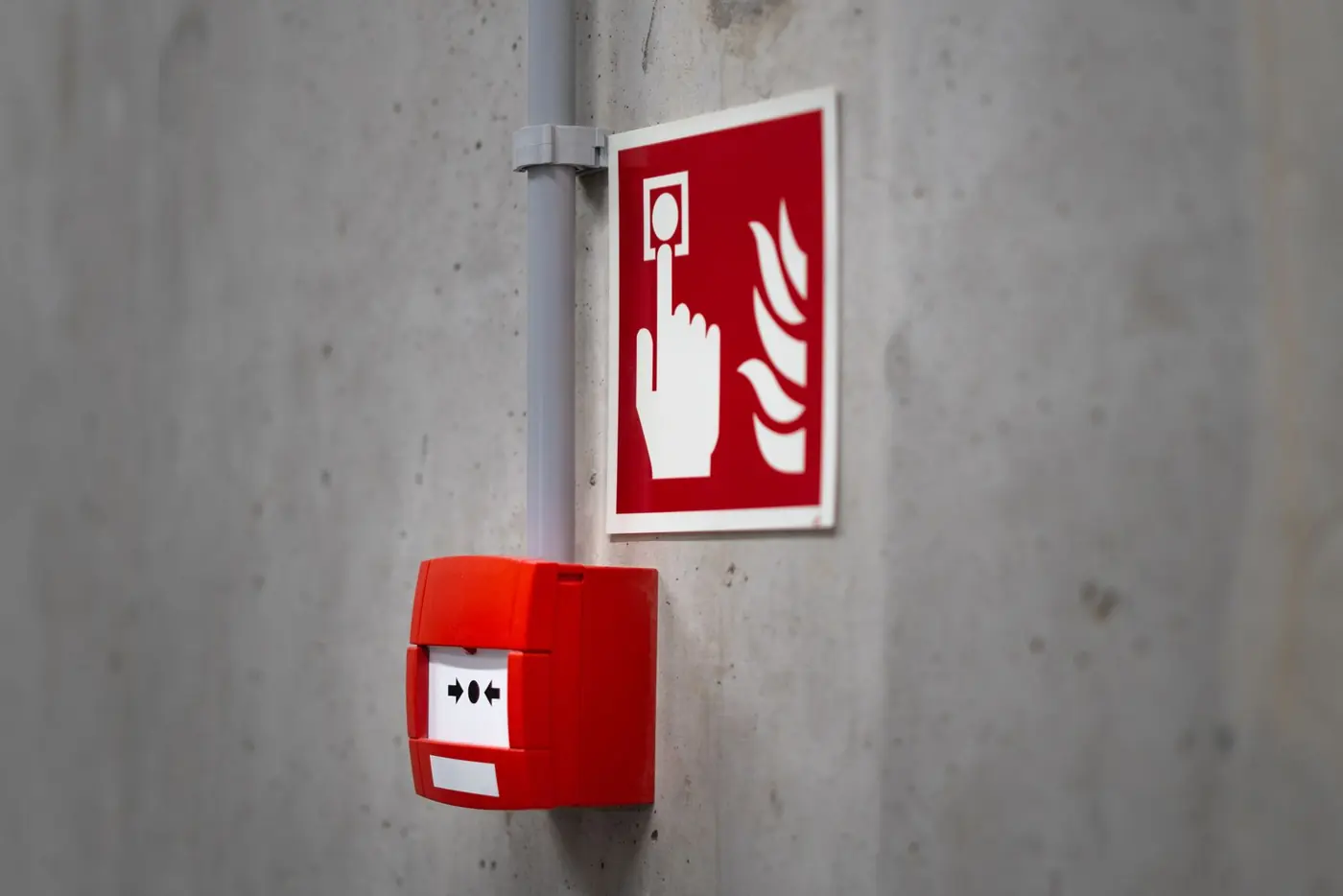 Red fire alarm manual call point and sign mounted on a concrete wall